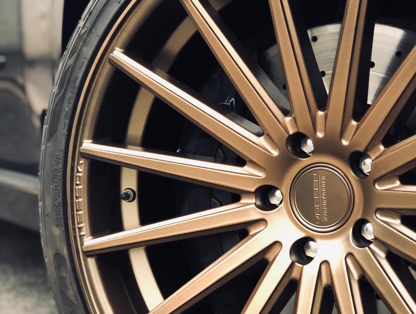 Bronze-colored car wheel with multiple spokes, black tire, and visible brake disc.