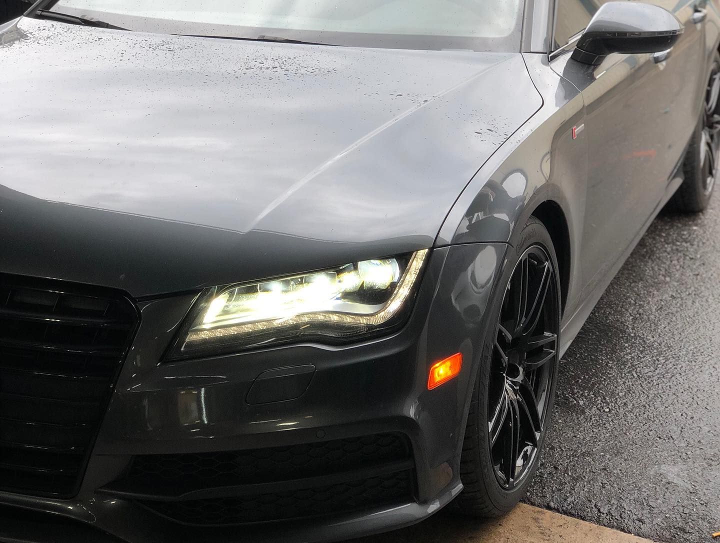 Dark gray Audi car, front view, headlights on, parked outside.