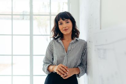A woman in a striped shirt is leaning against a wall.
