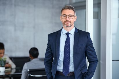 A man in a suit and tie is standing in an office with his hands in his pockets.