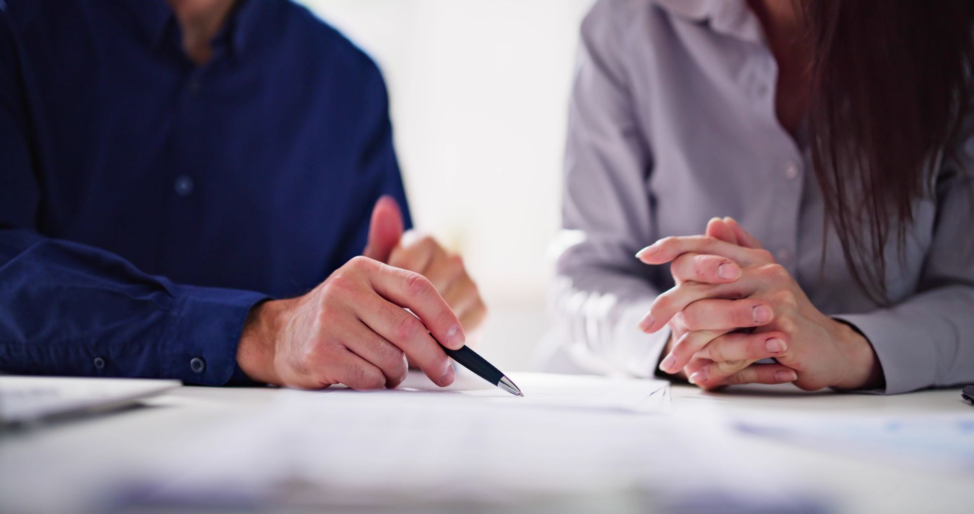 A man and a woman are sitting at a table with papers and a pen.