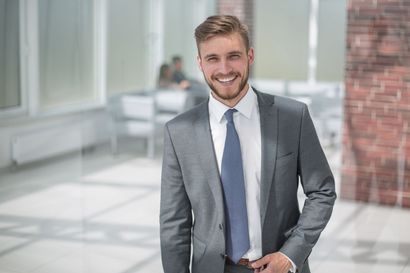A man in a suit and tie is standing in an office and smiling.