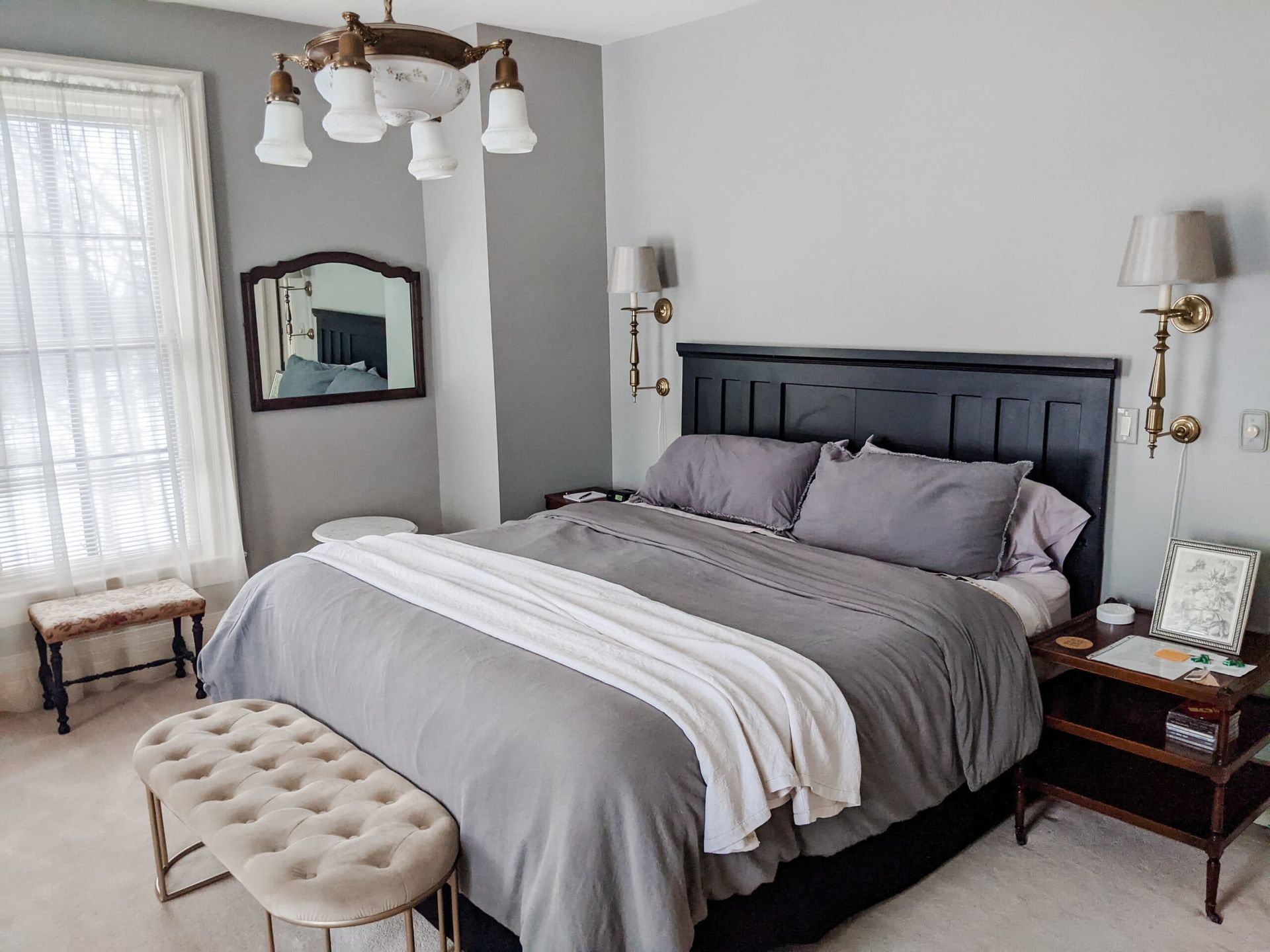 A bedroom with a large bed , a bench , a mirror and a chandelier.