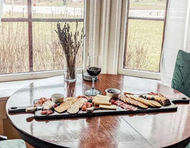 A table with a cutting board filled with food and a glass of wine.