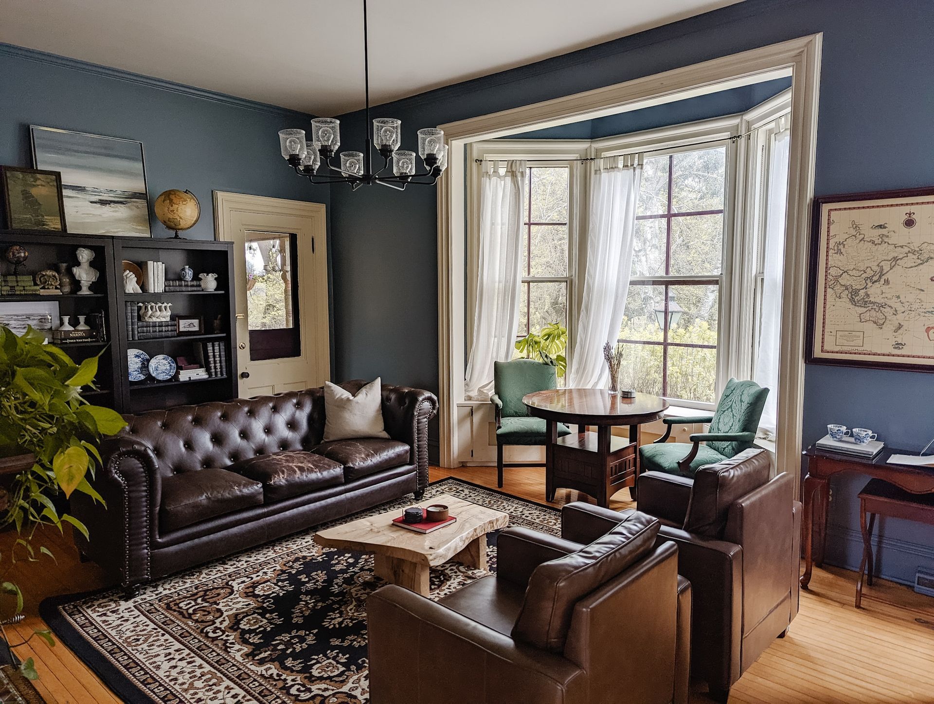 A living room with a couch , chairs , a table and a map on the wall.