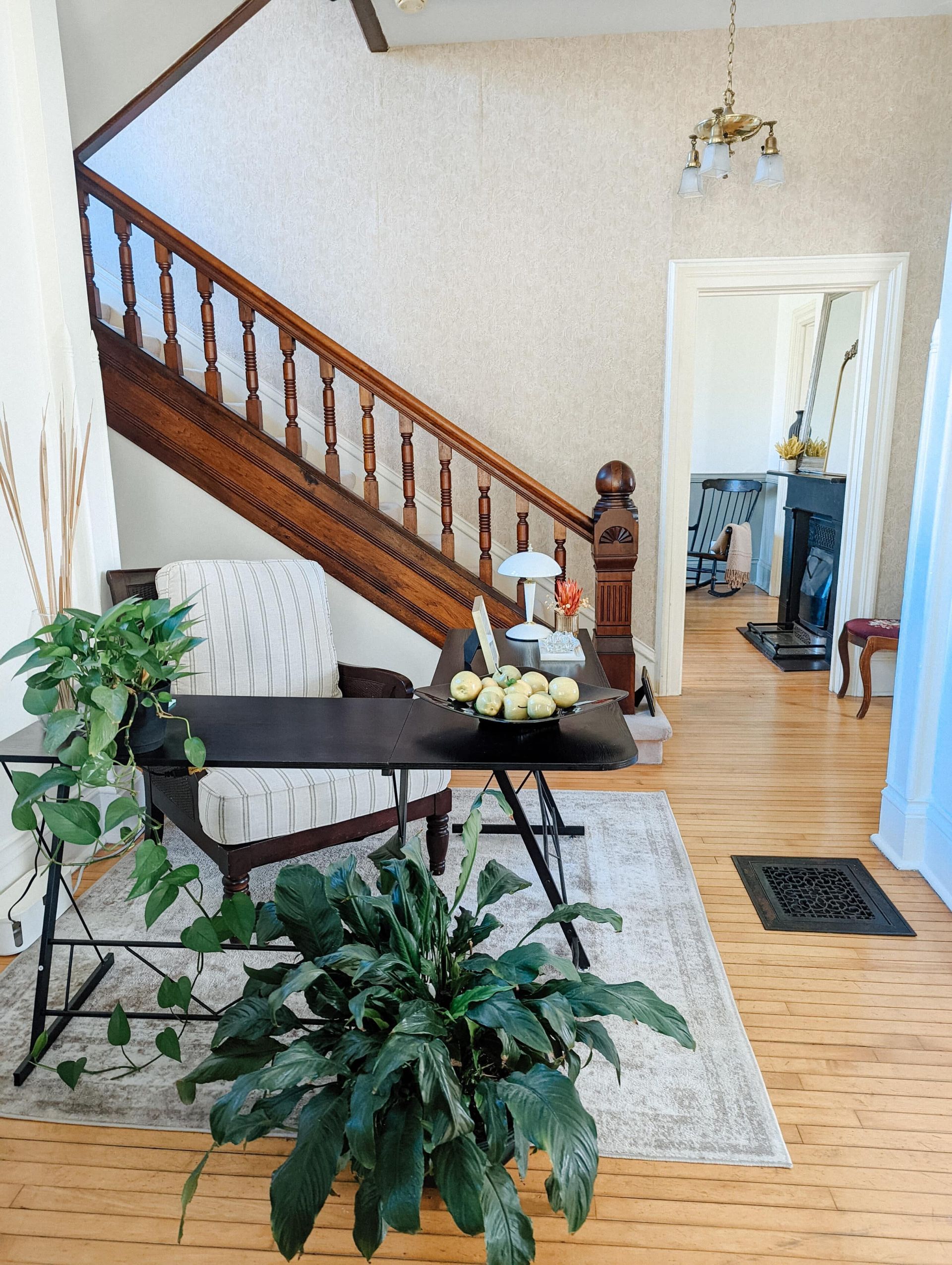 A living room with stairs , a desk , a chair and a plant.