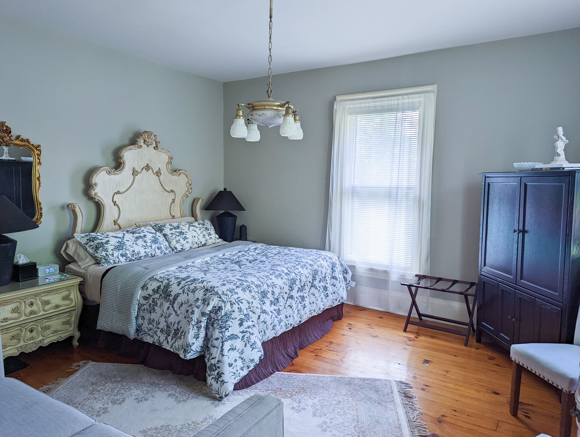 A bedroom with a large bed , dresser , nightstand , chair and window.