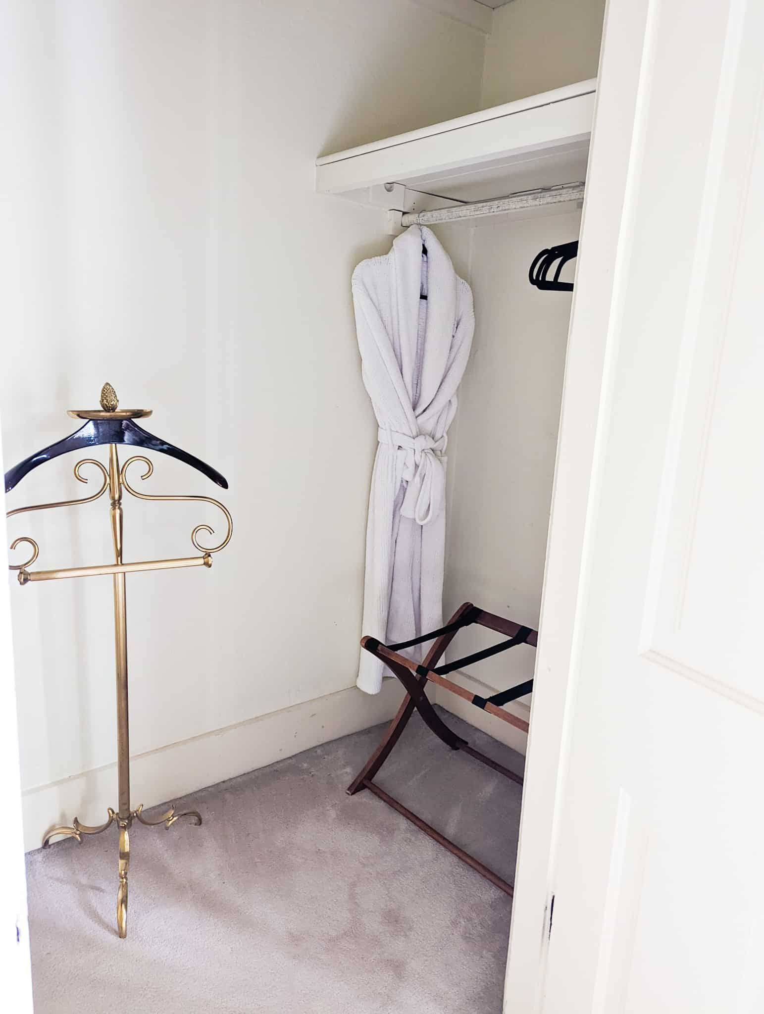 A white robe is hanging in a closet next to a suit rack.
