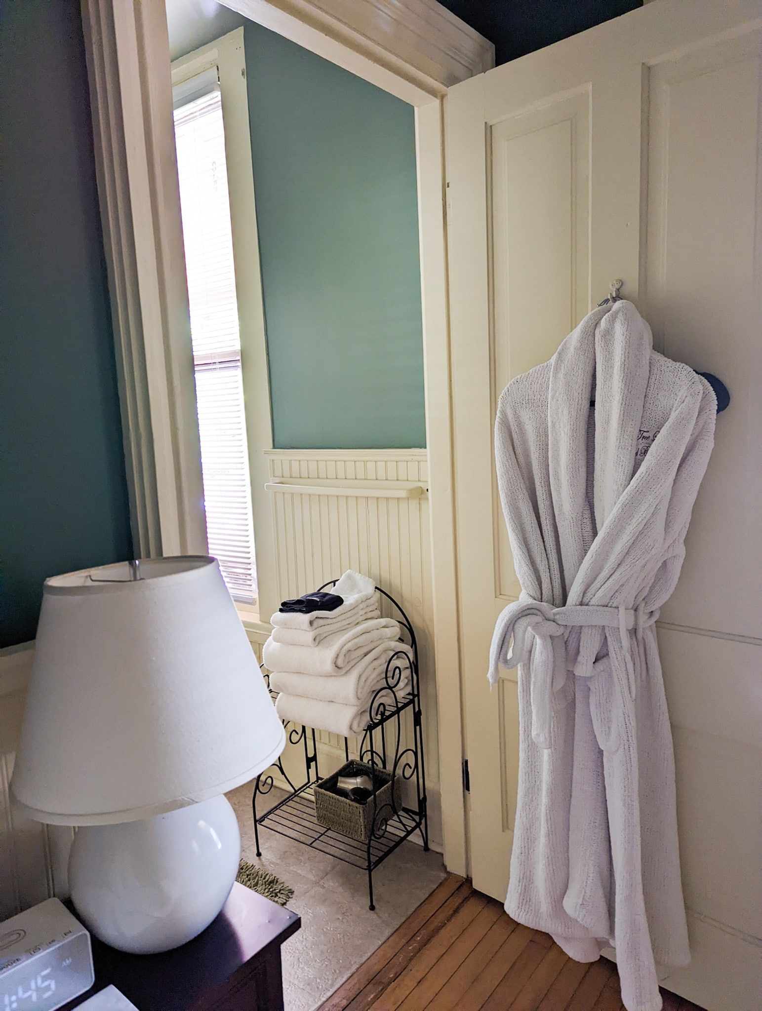 A white robe is hanging on a door in a bathroom next to a lamp.