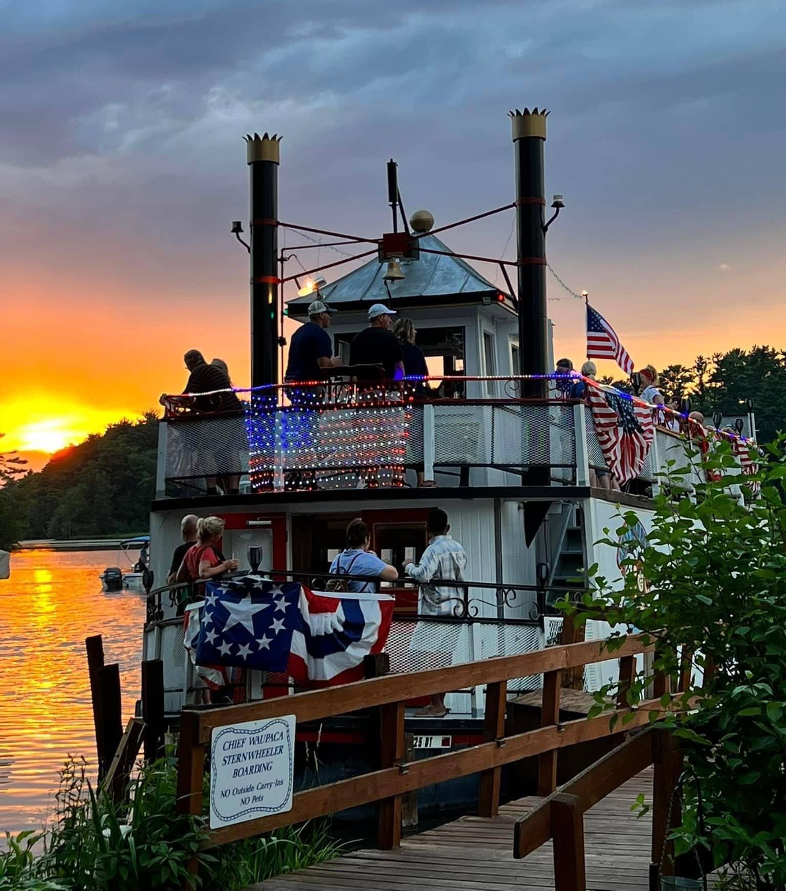A boat with american flags on the deck is docked at a dock at sunset.