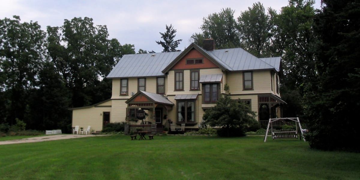 A large house with a metal roof sits in the middle of a lush green field