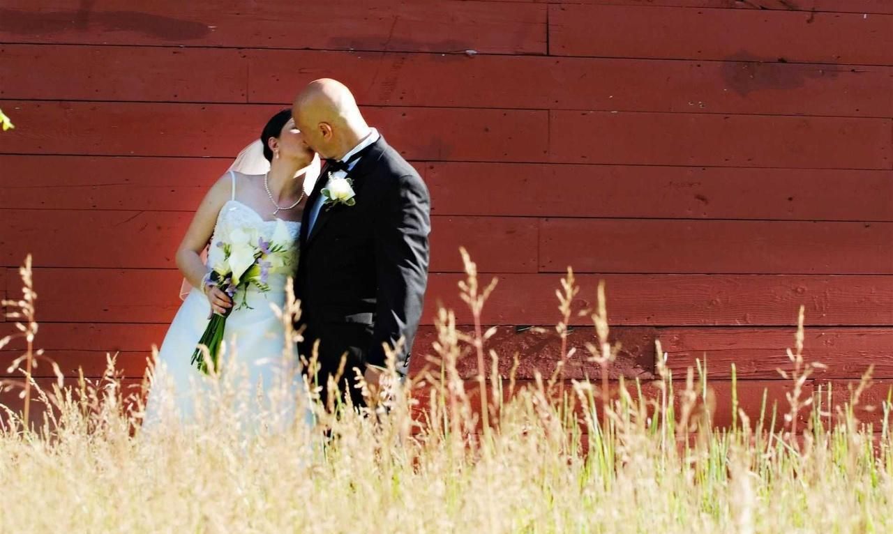 A bride and groom kissing in front of a red barn