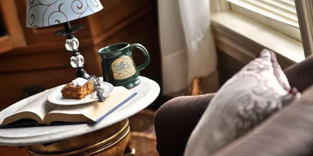A table with a book , a cup , and a muffin on it.