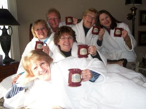 A group of people laying on a bed holding coffee mugs