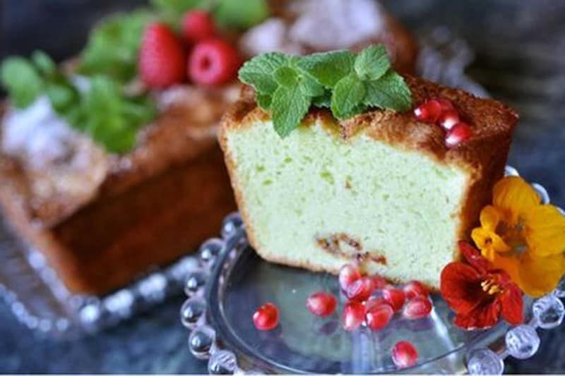 A slice of cake with mint leaves and pomegranate seeds on a glass plate.