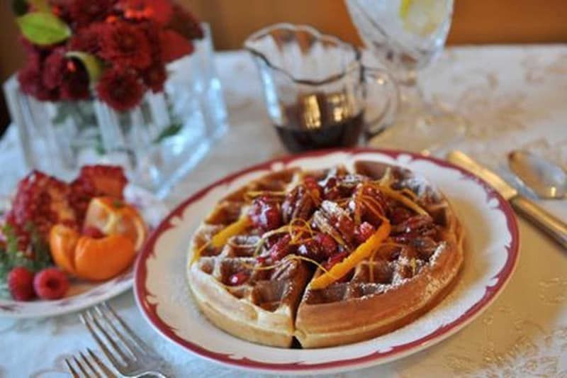A plate of waffles with berries and syrup on a table.