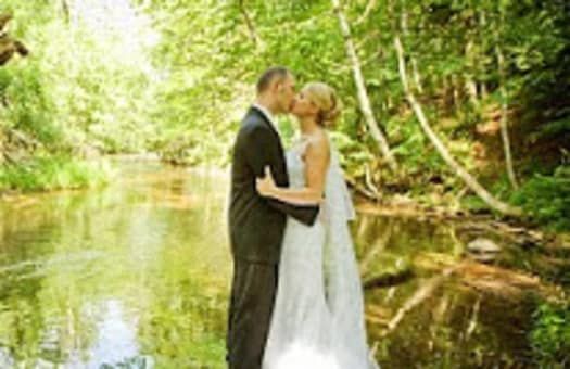 A bride and groom are kissing in front of a river.