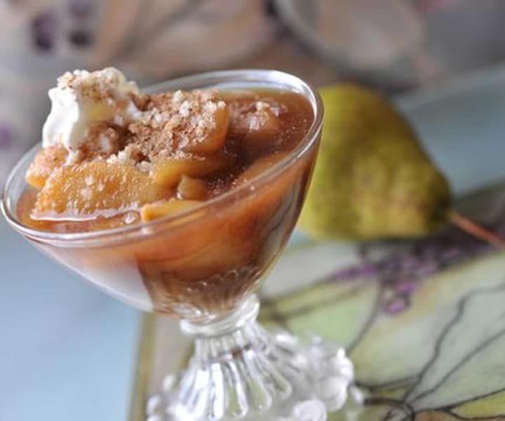 A glass bowl filled with a dessert next to a pear