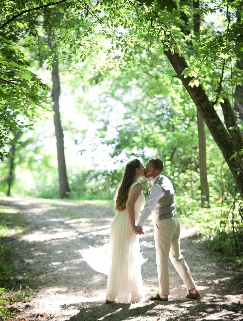 A bride and groom are kissing under a tree in the woods.