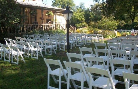 A row of white folding chairs are set up for a wedding ceremony.