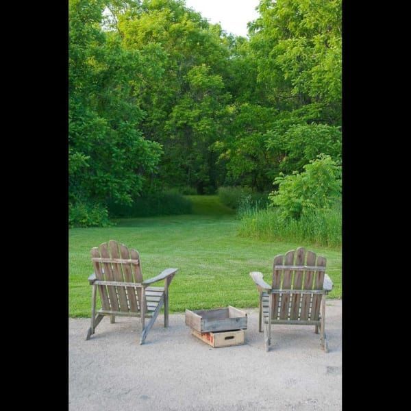 Two wooden chairs sit on a patio next to a fire pit