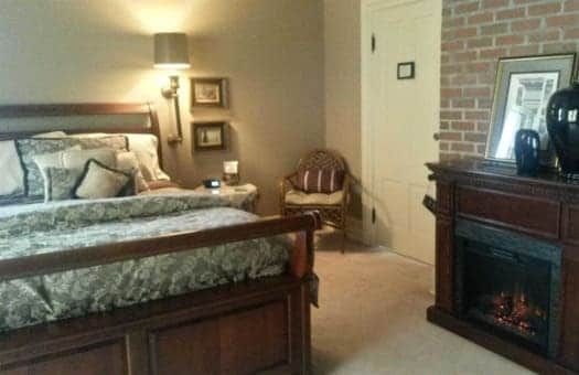 A bedroom with a bed , dresser , chair and fireplace.