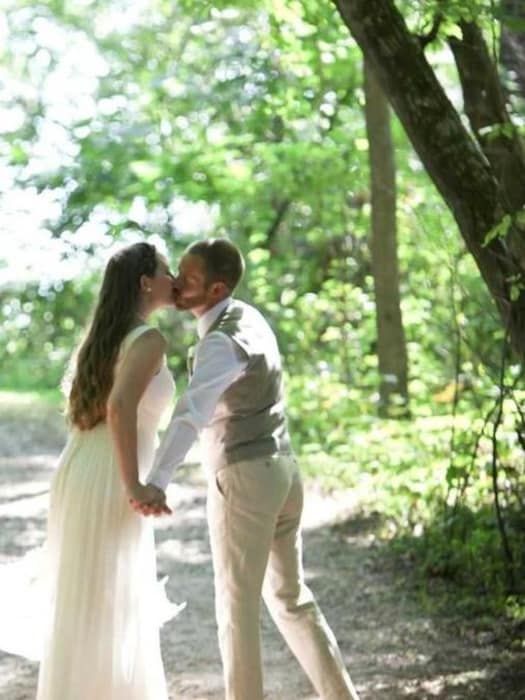 A bride and groom are kissing on a path in the woods.