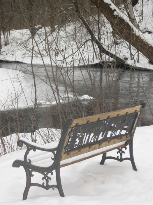 A park bench in the snow with a river in the background
