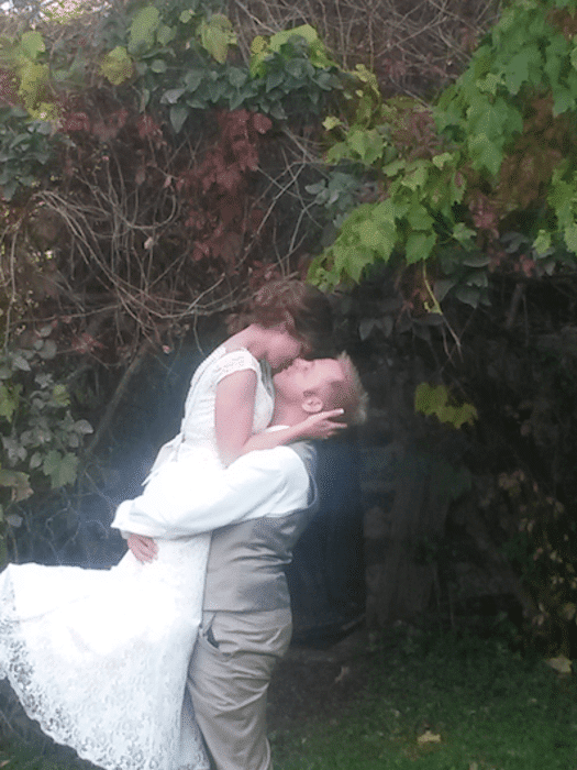 A man is holding a bride in his arms and kissing her.