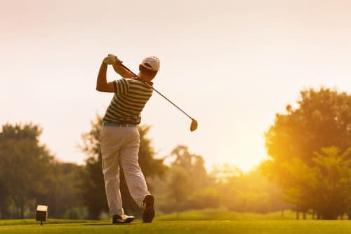 A man is swinging a golf club on a golf course at sunset.