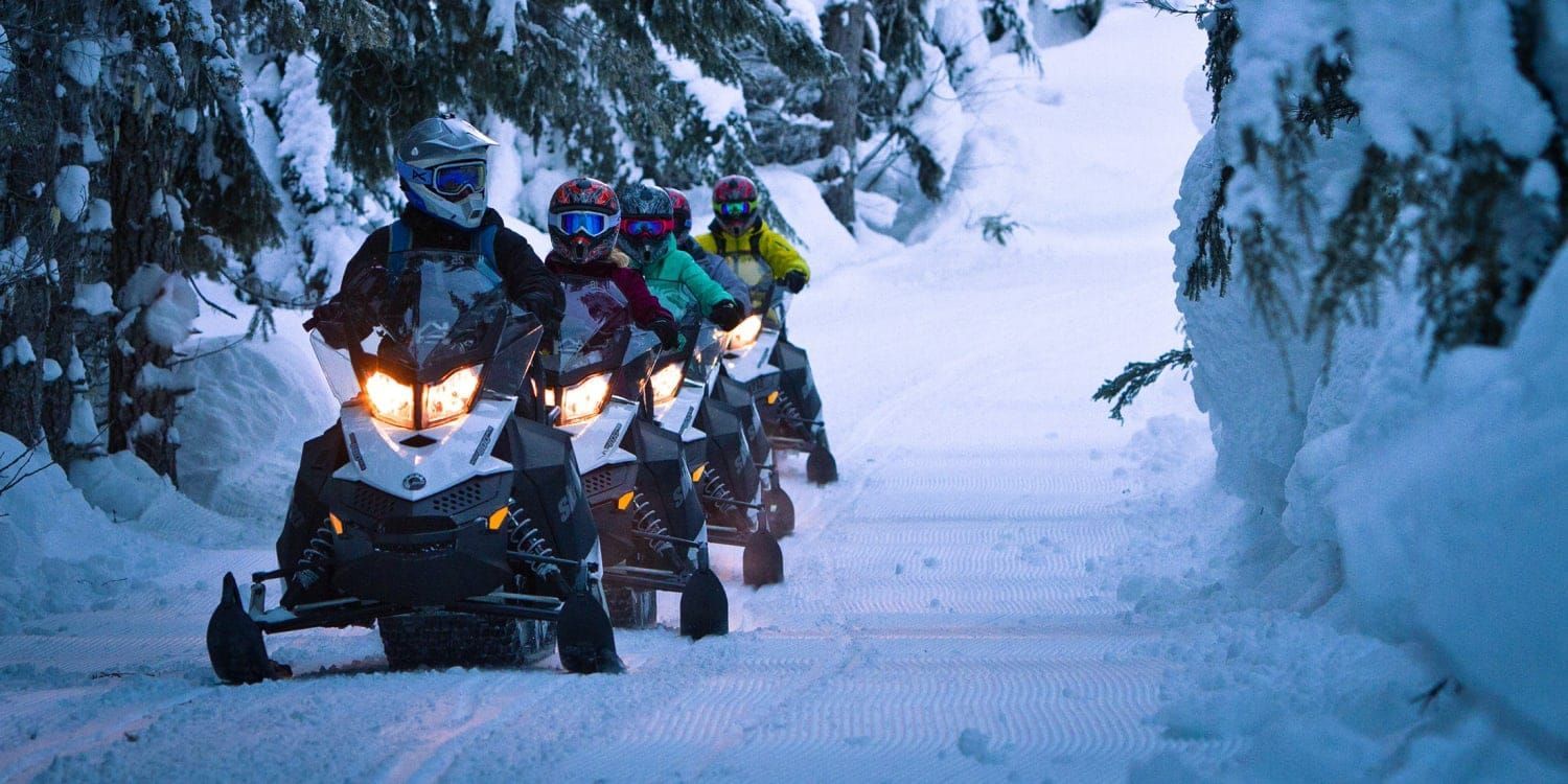 A group of people are riding snowmobiles down a snowy road.