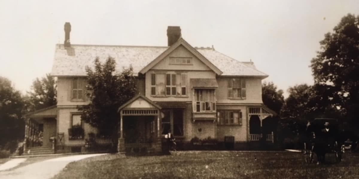 A black and white photo of a large house with a car parked in front of it.