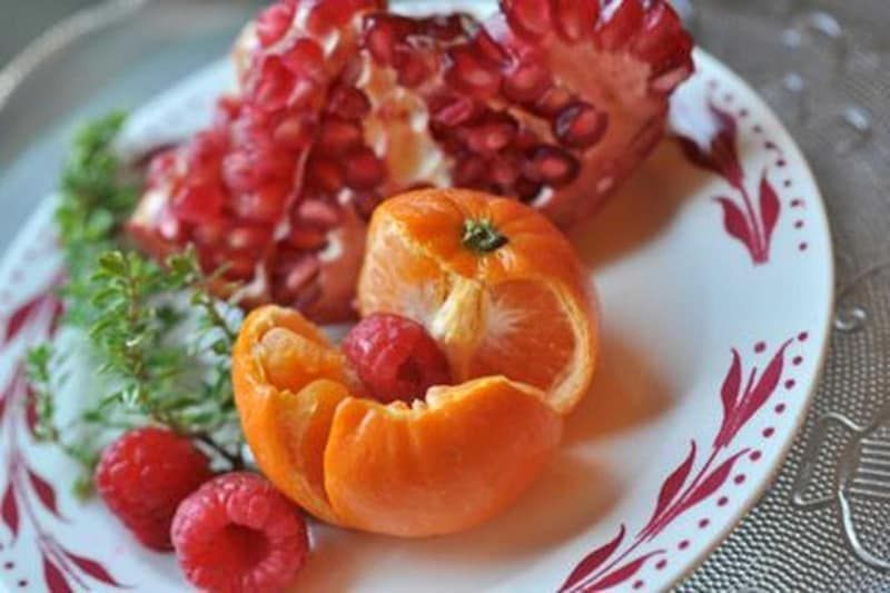A white plate topped with raspberries an orange and a pomegranate.