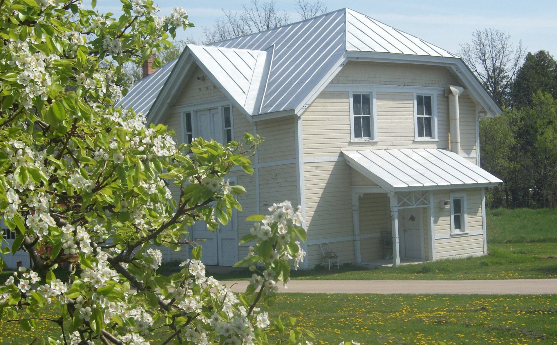 A white house with a metal roof is surrounded by flowers