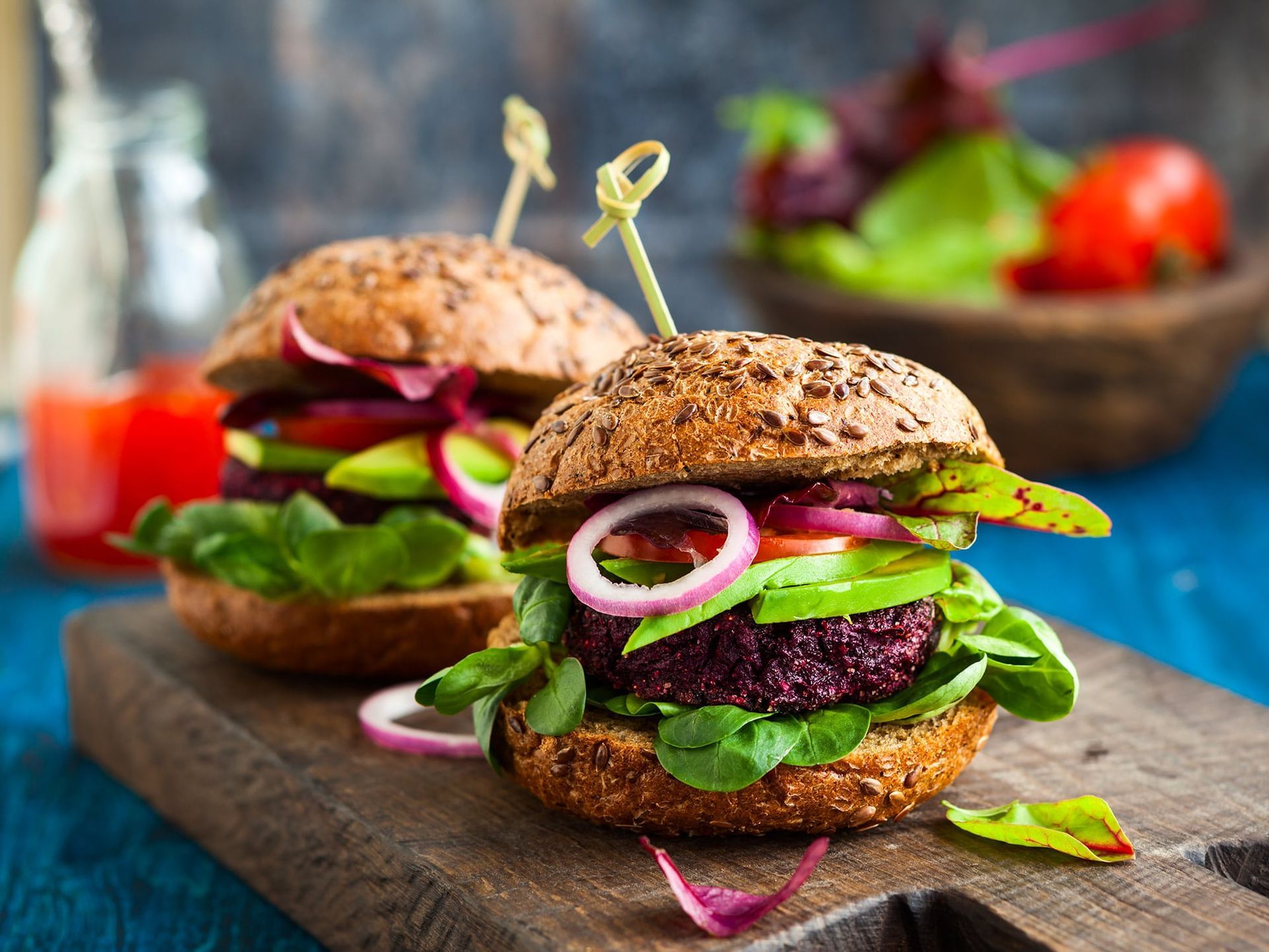 A close up of two burgers on a wooden cutting board.