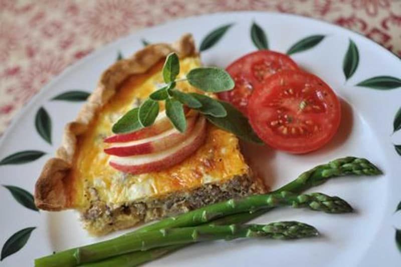 A white plate topped with a quiche , asparagus and tomatoes.
