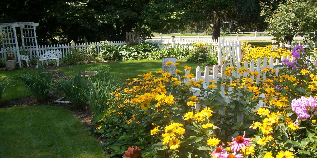 A garden with lots of flowers and a white picket fence