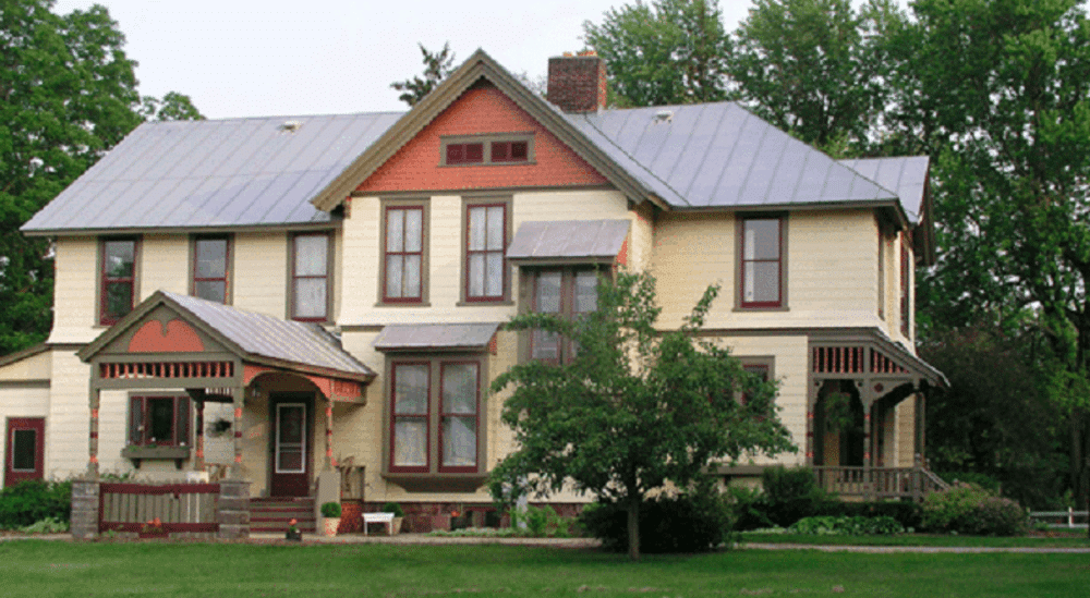 A large house with a metal roof is surrounded by trees