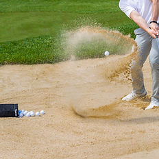 A man is hitting a golf ball out of a bunker on a golf course.