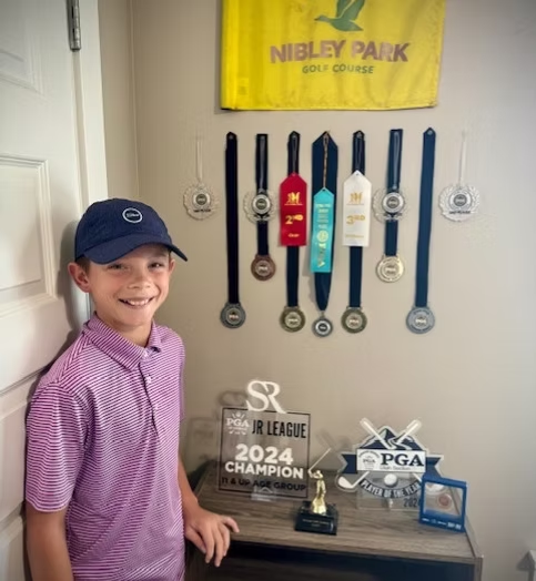 A young boy is standing in front of a trophy that says 2024 champion