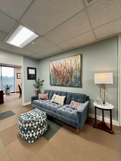 A living room with a couch , ottoman , lamp and painting on the wall.