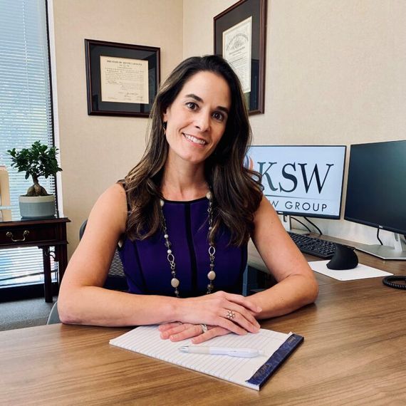 A woman is sitting at a desk with a computer and a sign that says ksw