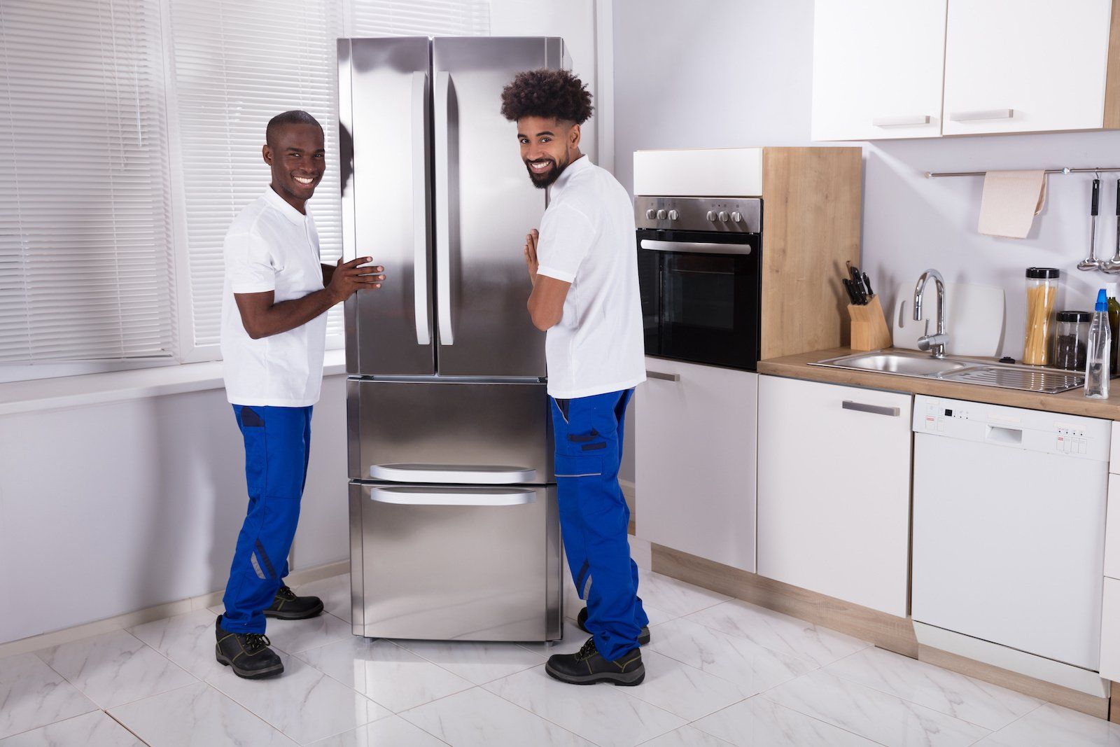 Two male movers in the kitchen, repairing the freezer.