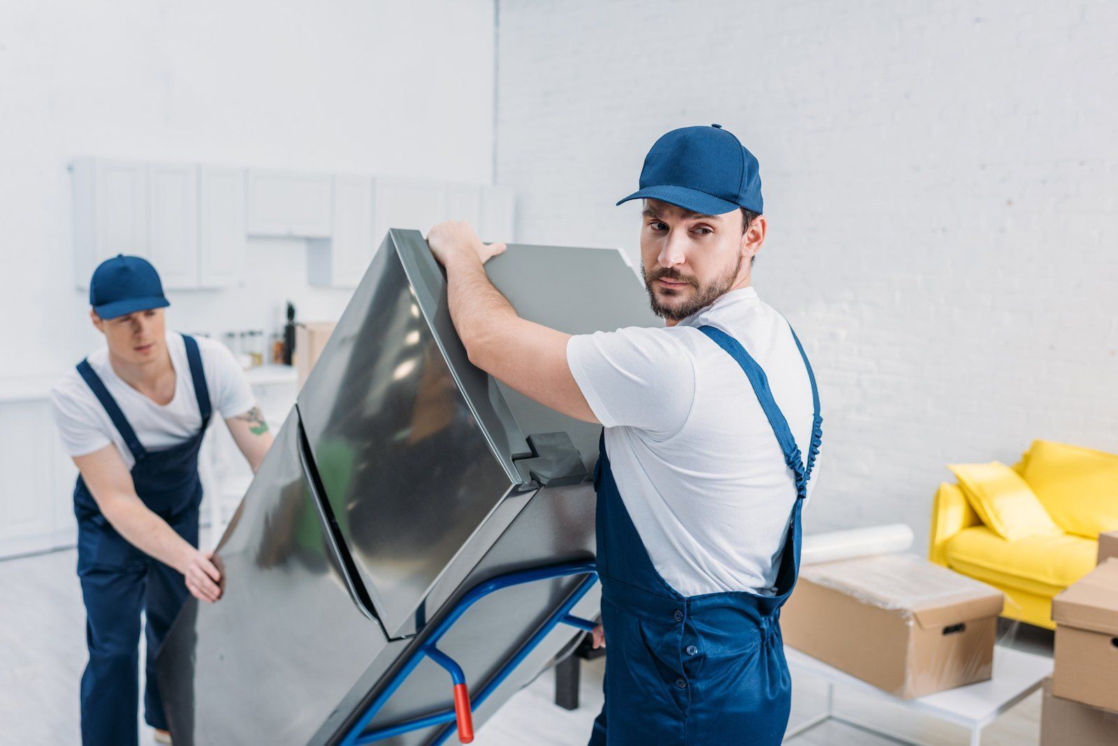 Movers using a hand truck to carefully transport a refrigerator within an apartment.