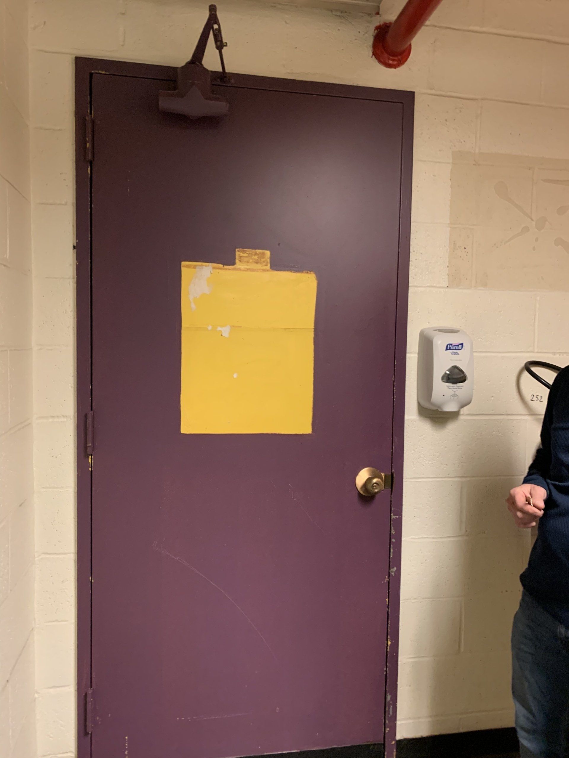 Purple door with yellow paper, a hand sanitizer dispenser, and a person partially visible.
