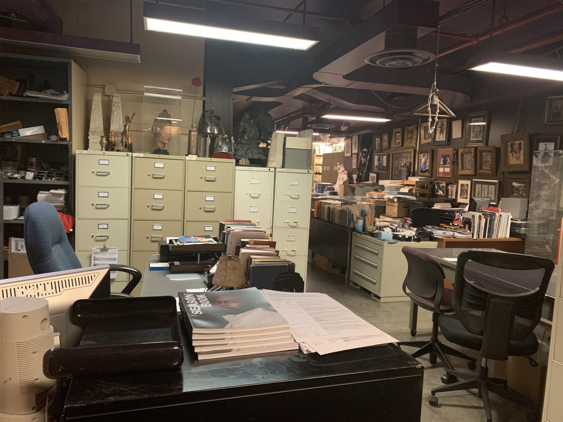 An office with beige filing cabinets, a desk, and various objects, including a desk with papers, is in view.