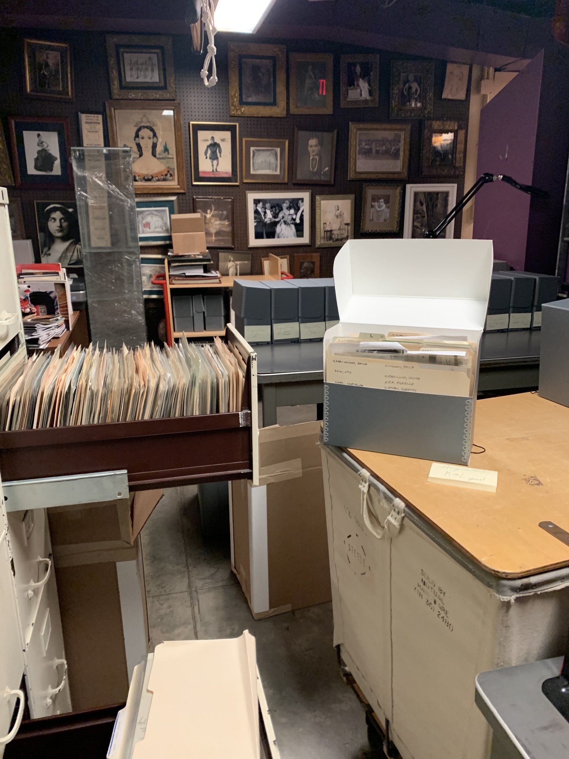 A cluttered room with old records, files, and framed photos on walls and shelves.