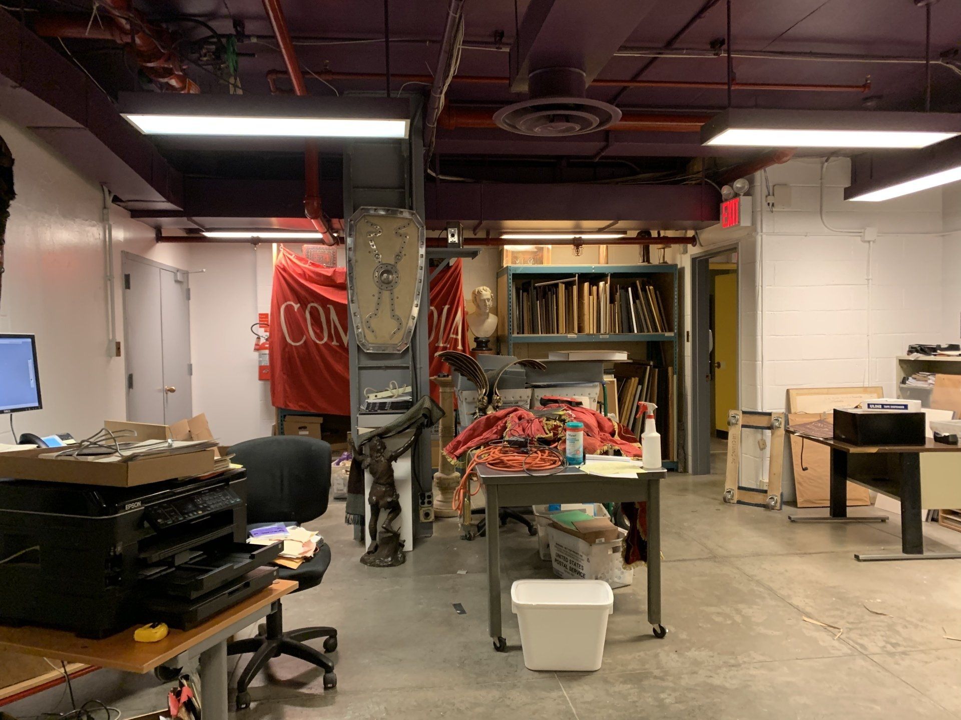 An art studio with work tables, a red banner, and various art supplies scattered about.