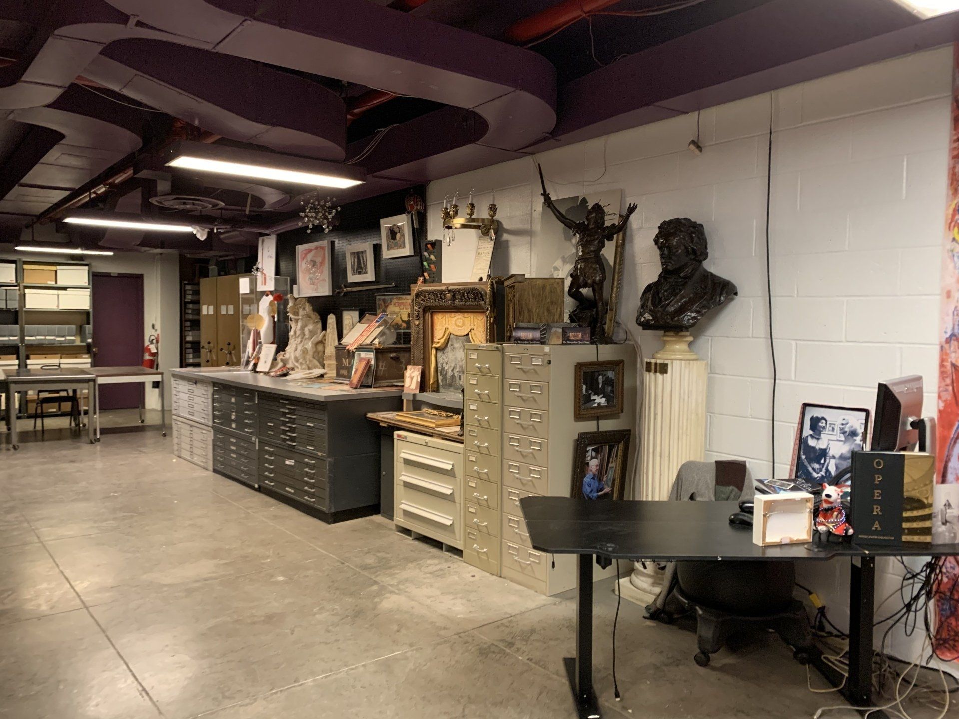 An art studio interior with sculptures, busts, and artwork displayed on tables and shelves.
