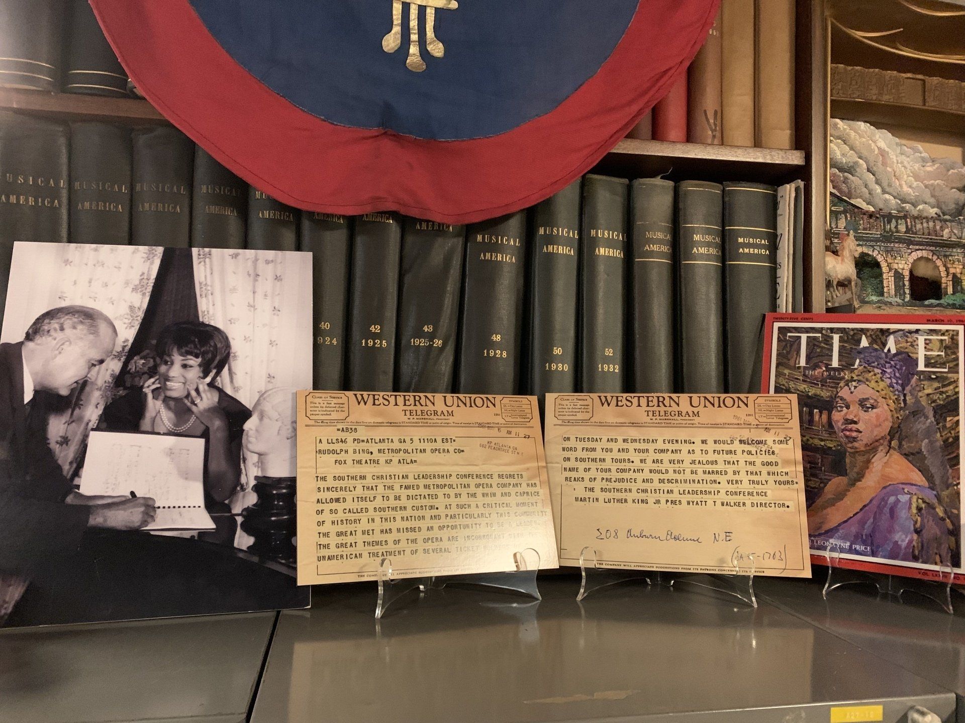 Display of historical items: photo, letters, book spines, art, and a flag.